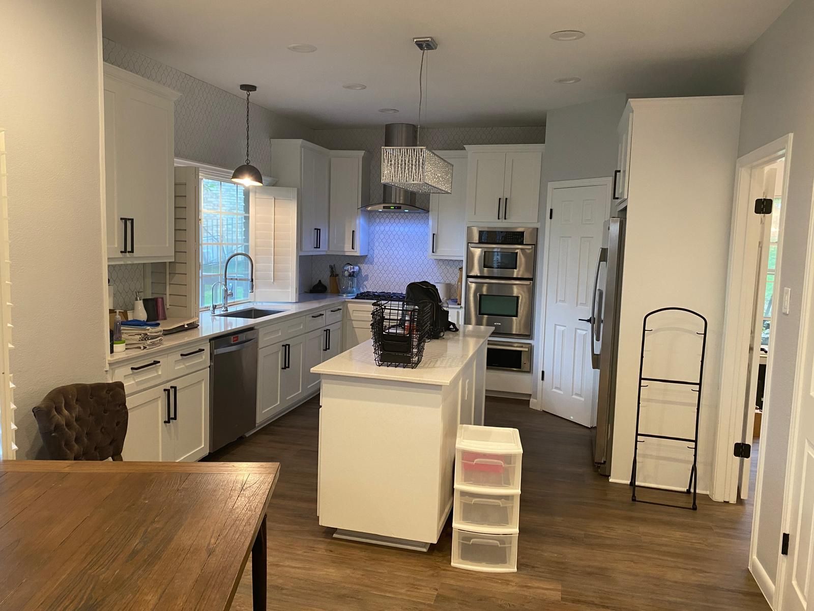 A white kitchen with wooden floors, a center island, stainless steel appliances, and a dining table in the foreground.