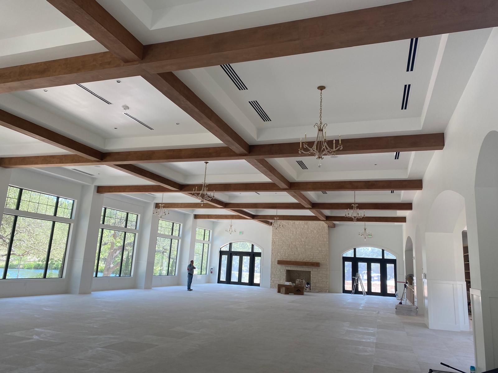 A large, open-concept room with white walls, a vaulted ceiling featuring decorative wooden beams, and multiple chandeliers.