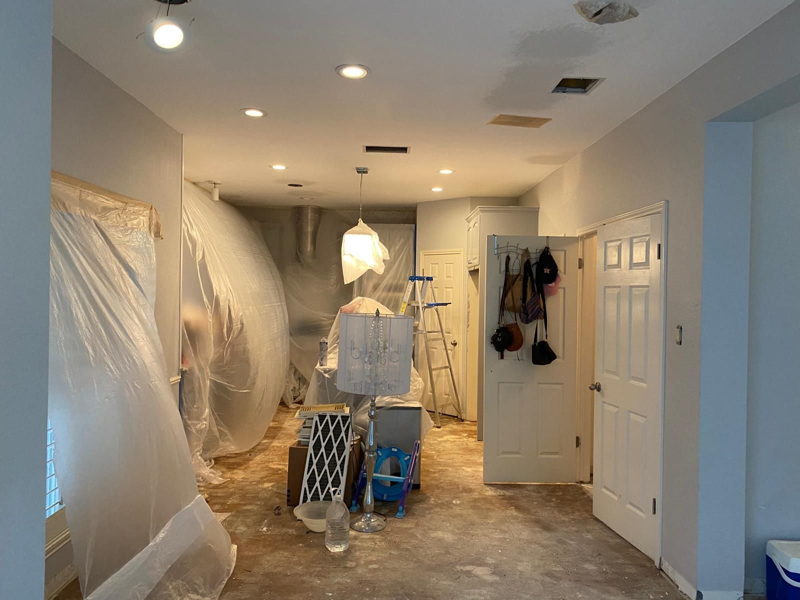 A residential room under renovation with walls covered in plastic sheeting, a central pendant light, and a white door.