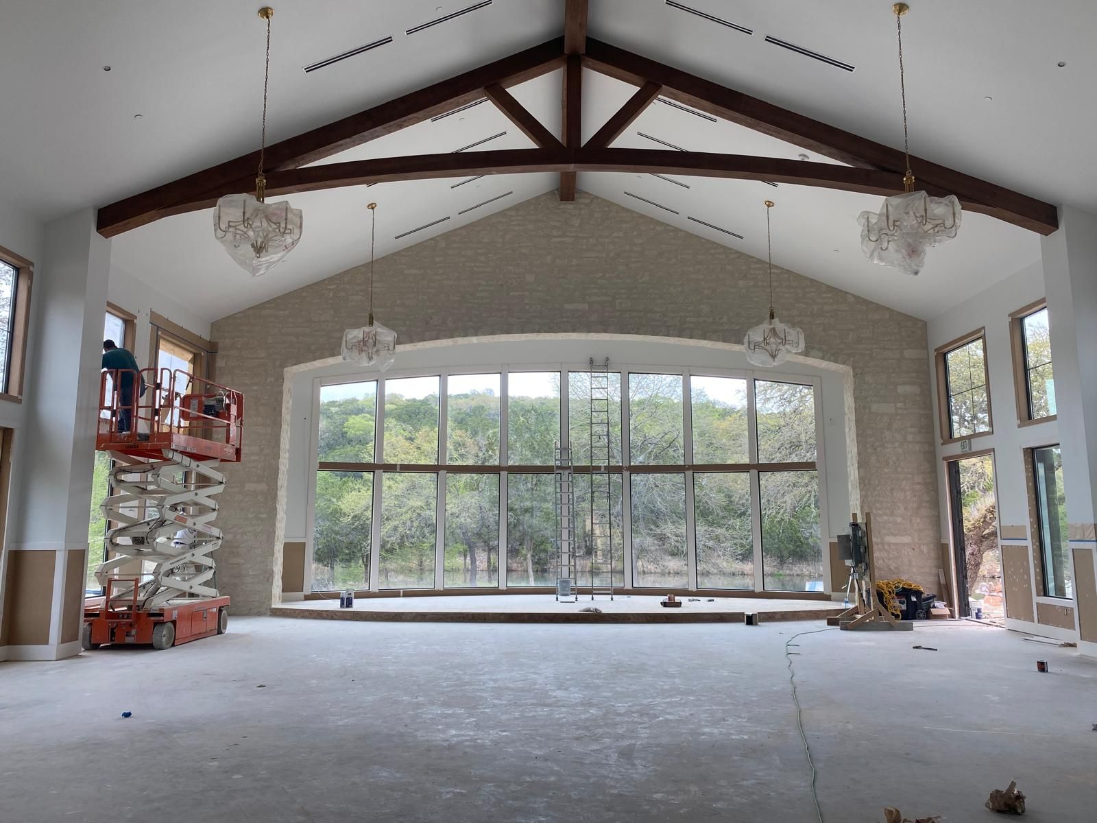 Construction workers use a scissor lift inside a large, high-ceilinged hall with stone walls and floor-to-ceiling windows.