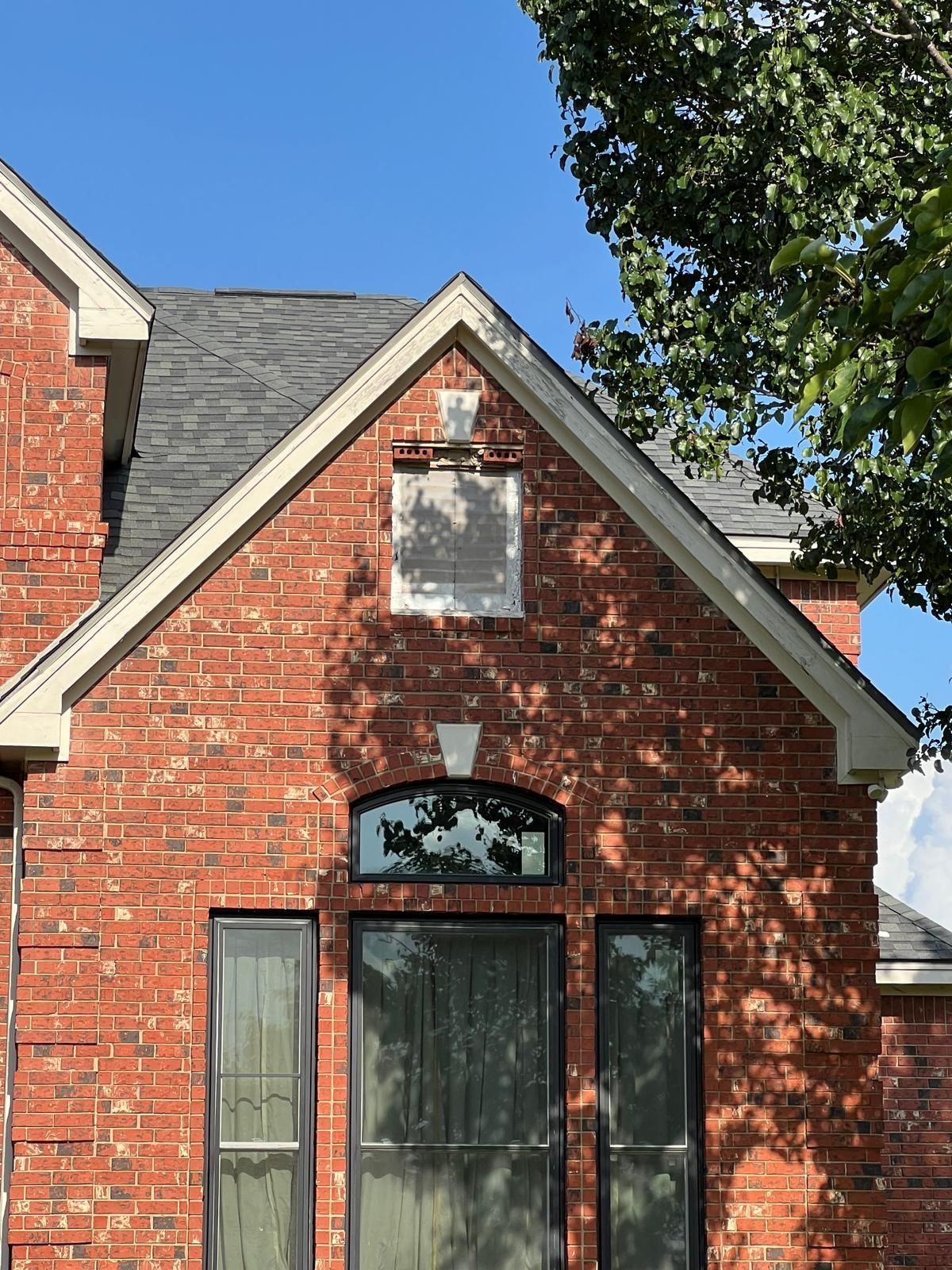 Red brick gable roof of a home featuring a decorative stone inset and a large arched window with black trim.