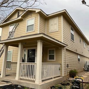 A two-story, yellow house with a white front porch and a ladder leaning against the left side.