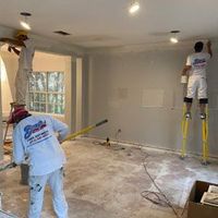 Three painters in company uniforms working on the ceiling and walls of an unfinished interior space.