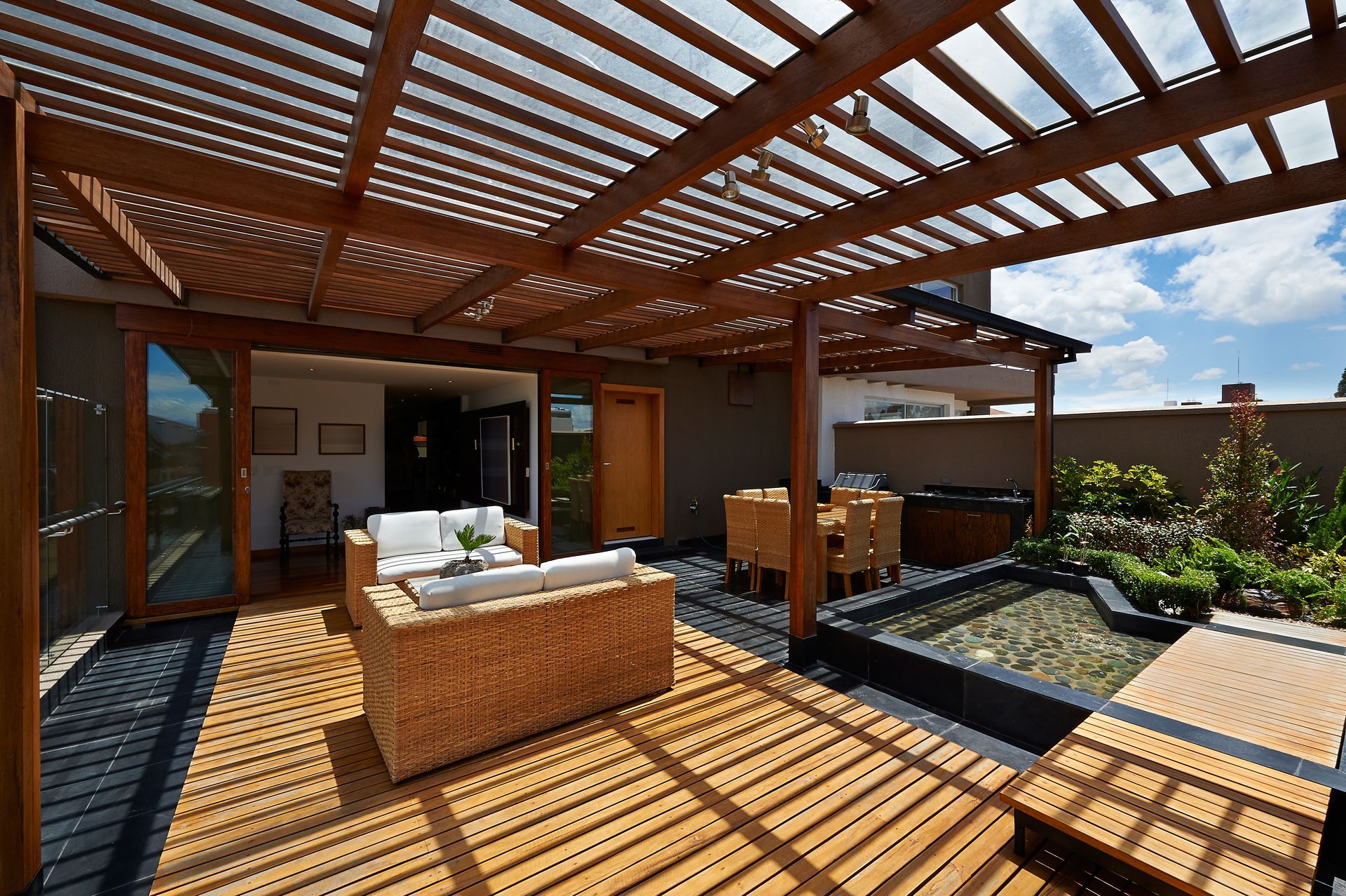 Sunlit rooftop patio with wicker seating, wooden pergola, and small garden beds