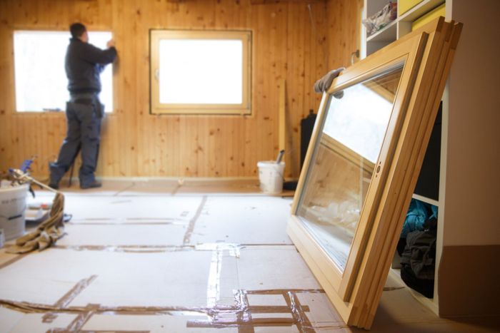 Worker installing a wood-paneled wall with a window in a room under renovation