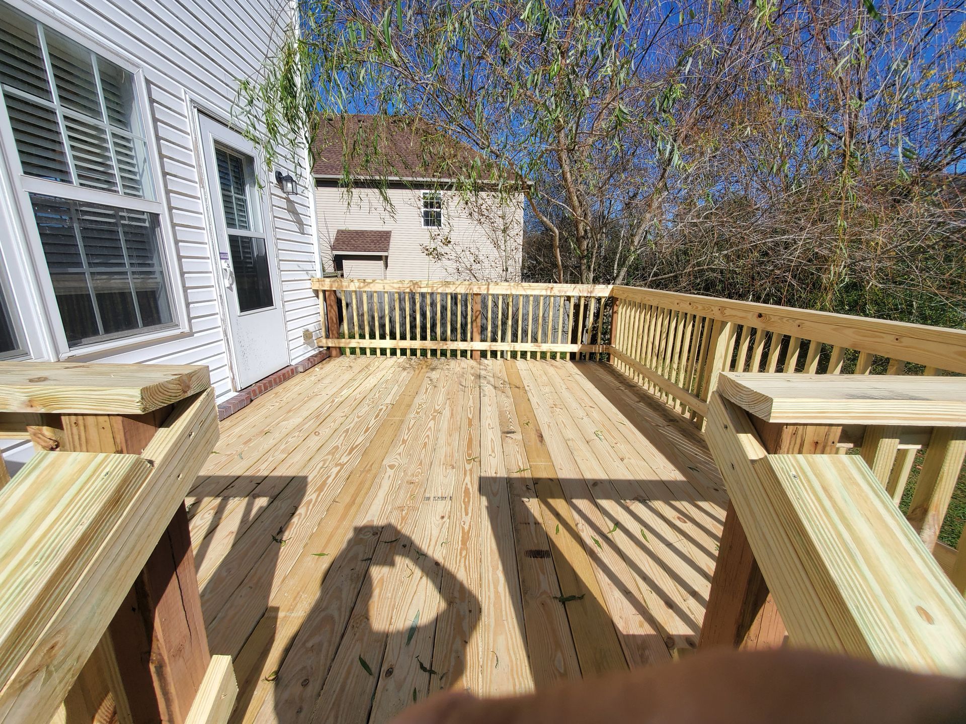 A person is standing on a wooden deck with a house in the background.