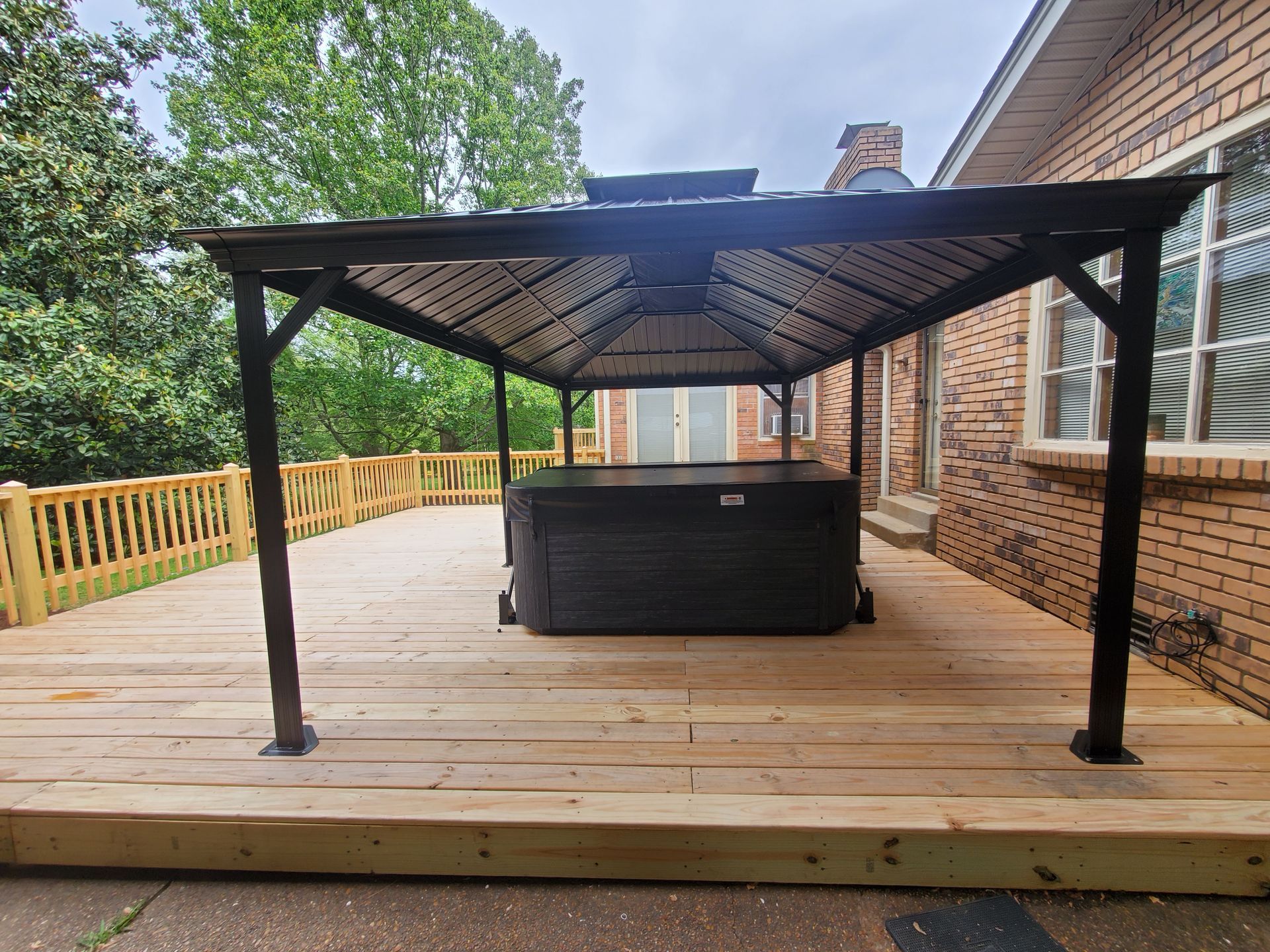 A hot tub is sitting under a gazebo on a wooden deck.