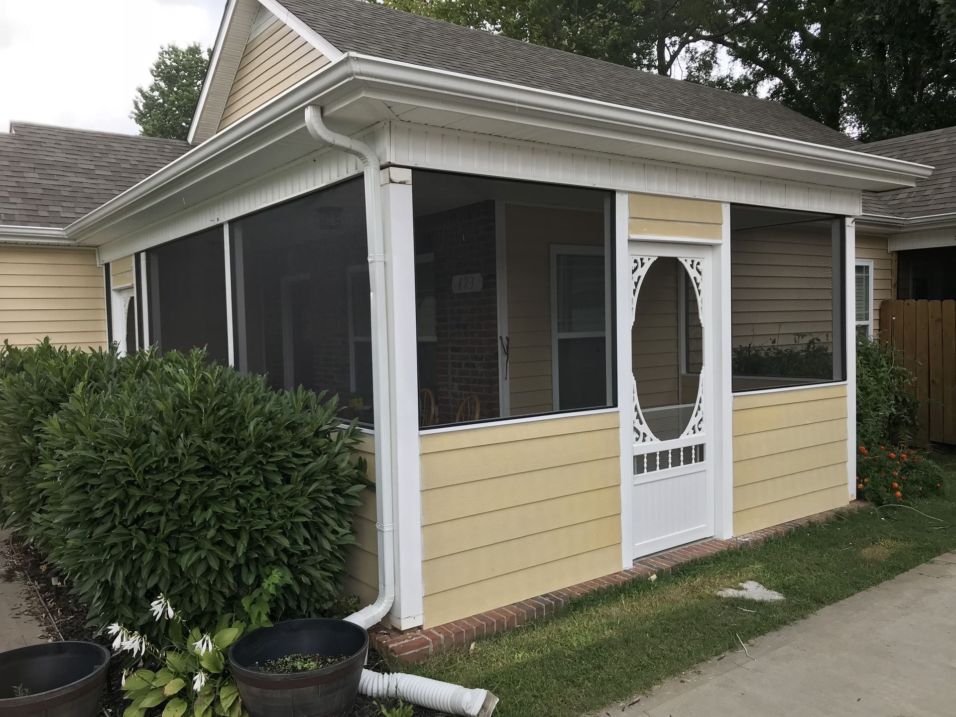 A yellow house with a screened in porch and a white door.