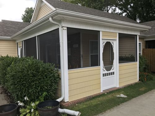 A yellow house with a screened in porch and a white door.