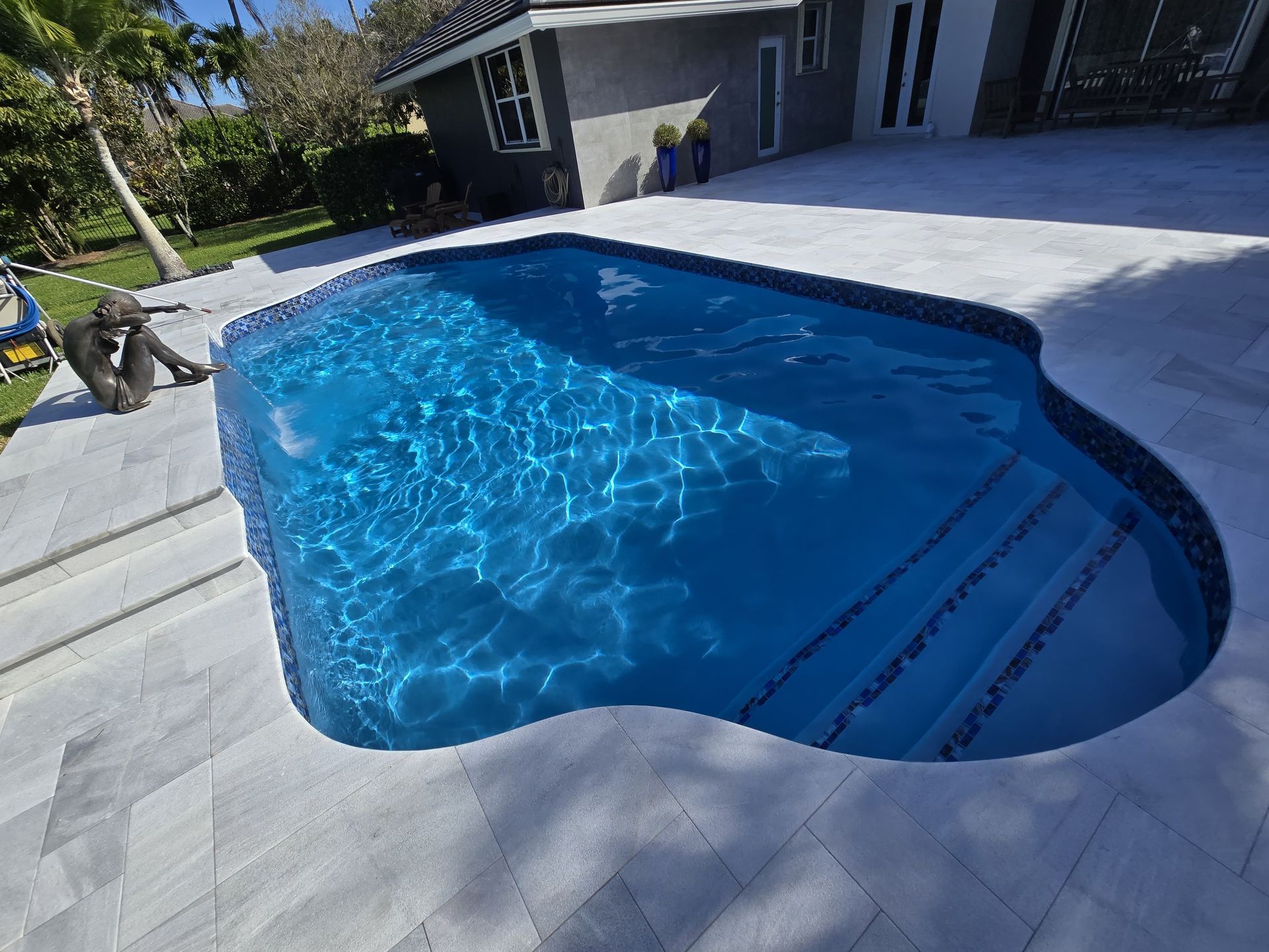 Pool with blue water, steps, and surrounding light gray stone patio.