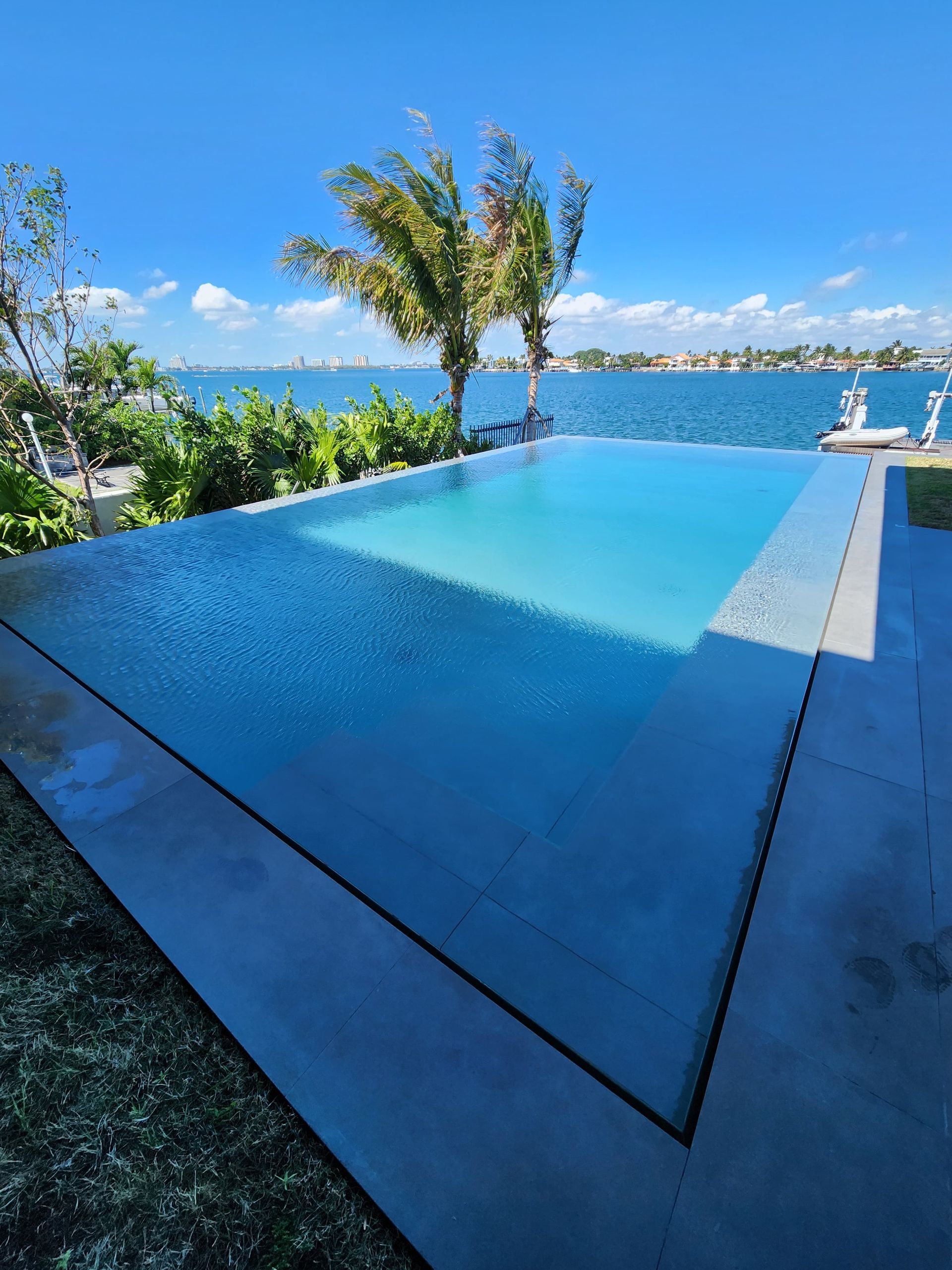 Infinity pool overlooking a bay with blue water, sunny sky, and palm trees.