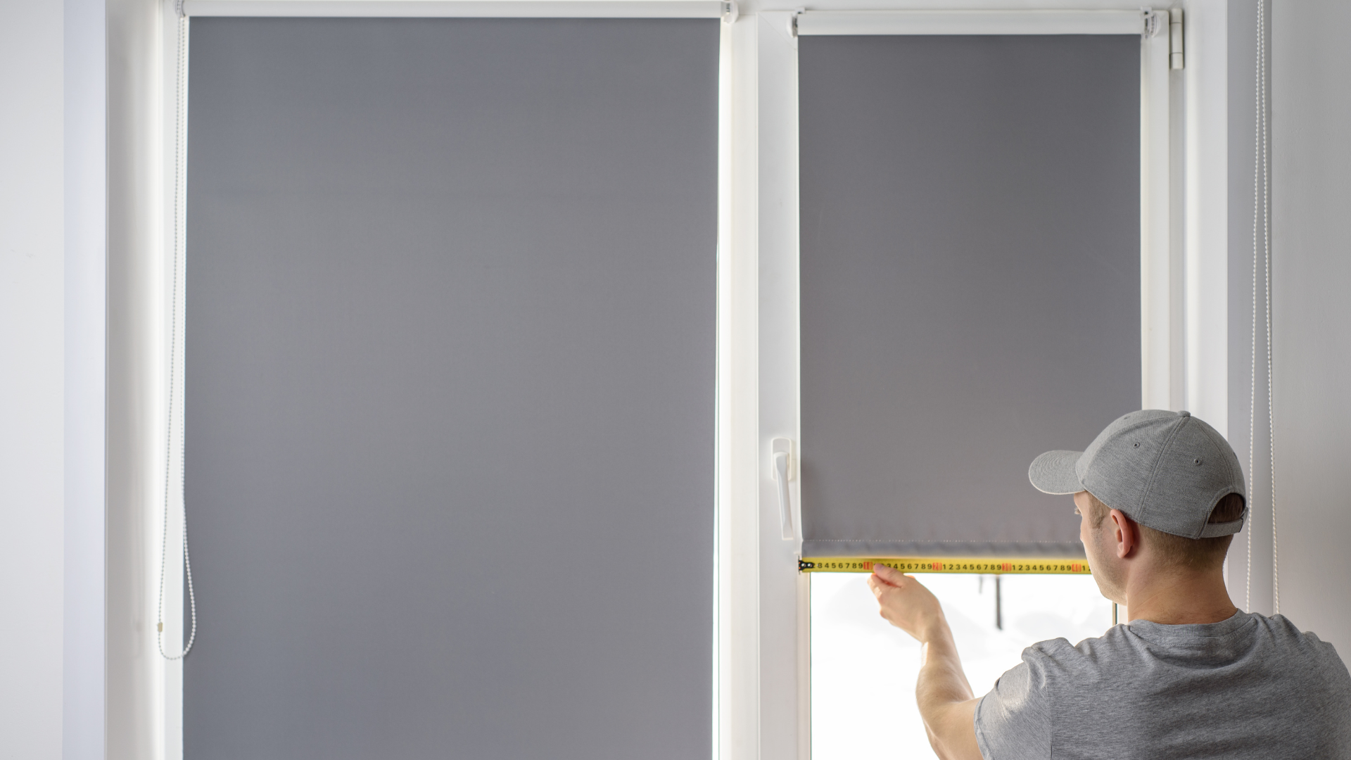 A man is measuring a window blind with a tape measure.
