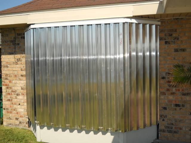 Metal corrugated hurricane shutters installed on a window, attached to a brick house.