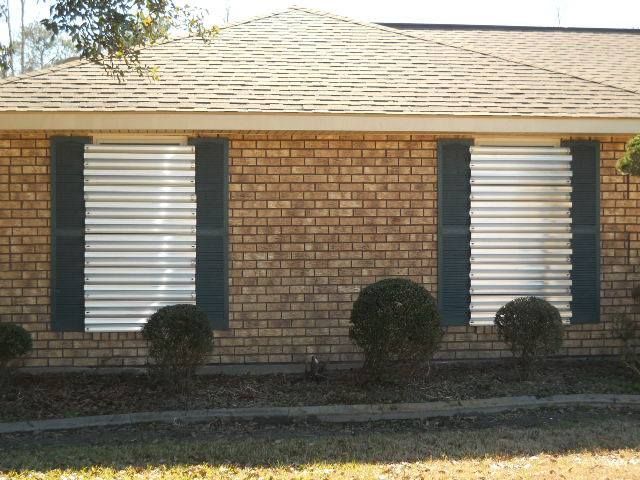 Brick house with corrugated metal window shutters and green shutters.