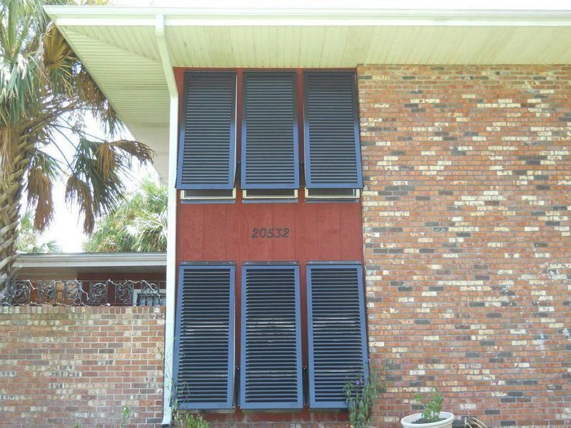 Red brick house with dark louvered shutters on a reddish-brown section of wall, with house number 25537.