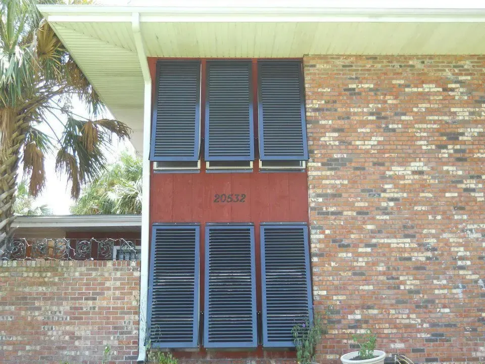 Brick building with six blue louvered shutters on a red panel; house number