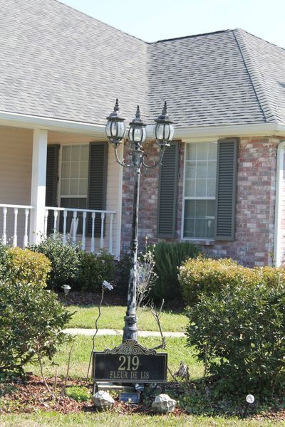 Black lamp post with address 219 in front of a house with shutters and bushes.