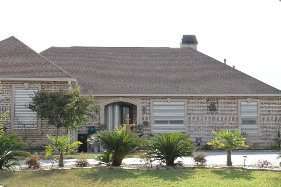 Brick house with brown roof, arched entryway, front yard with trees and grass.