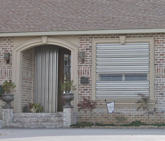 Exterior of a brick building with closed metal shutters over the window and open metal shutters over the entrance.
