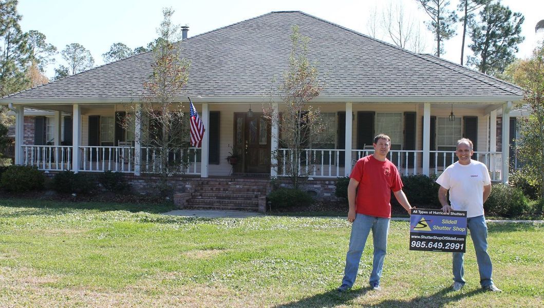 Two men standing in front of a house, holding a sign.