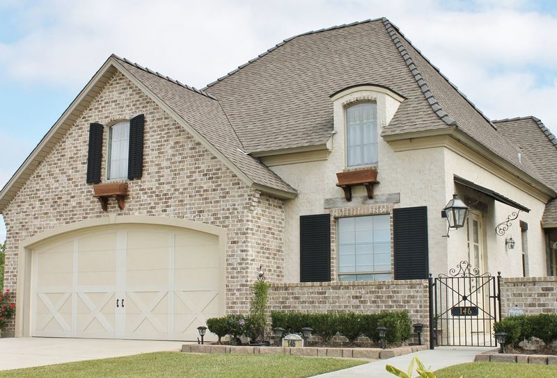 Brick house with beige garage door, black shutters, and tan roof.