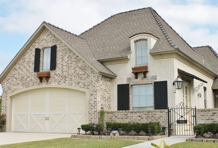 Tan brick house with a beige garage door, black shutters, and a wrought iron gate.