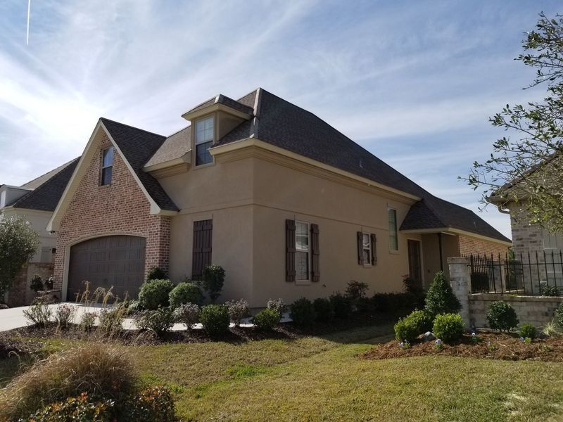 A two-story house with a brick facade and stucco siding on a sunny day.