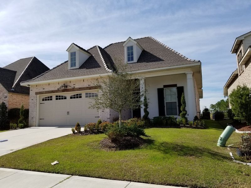 White house with brown roof, two dormers, garage, and front porch. Green lawn and blue sky.