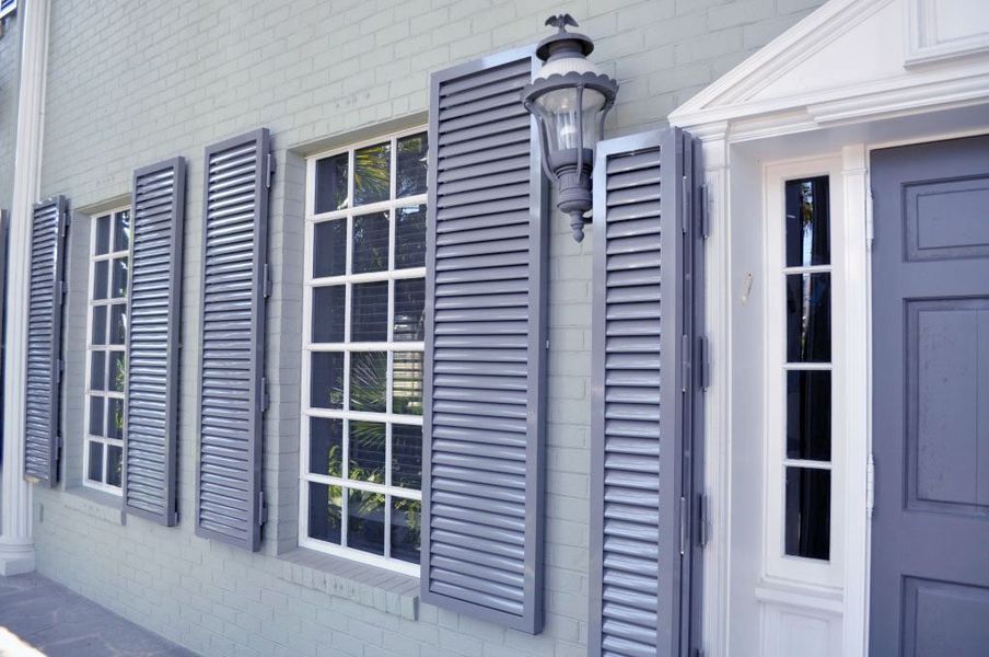 Gray shutters on a light green brick building with a white-framed window and a gray door.
