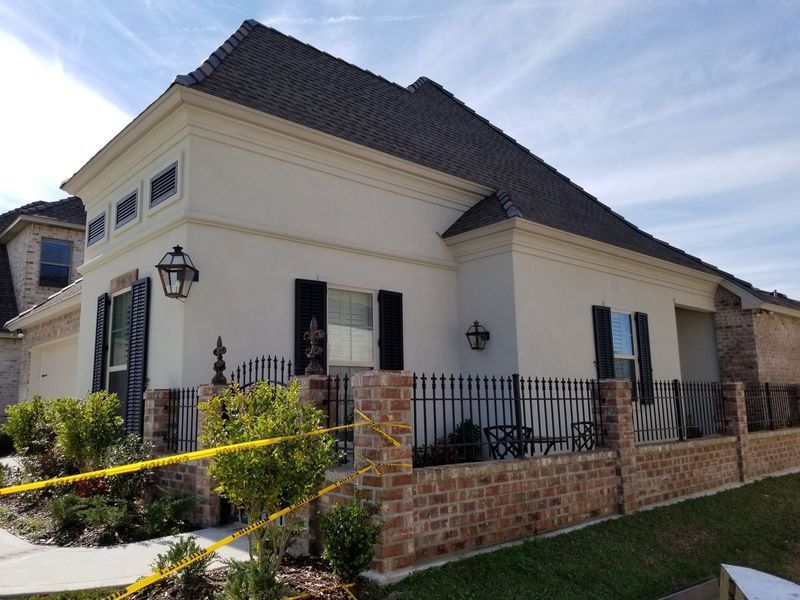 A cream-colored house with a brick base and black wrought iron fence on a sunny day.