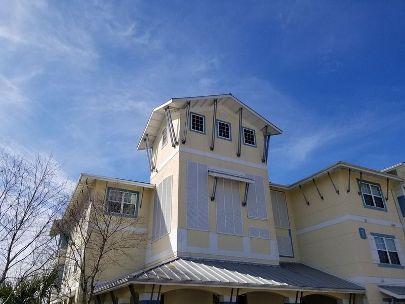 Yellow and white building with a tower against a blue sky, visible windows, and silver roof.