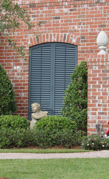 Brick building with blue shutters, green bushes, a statue, and a lawn.