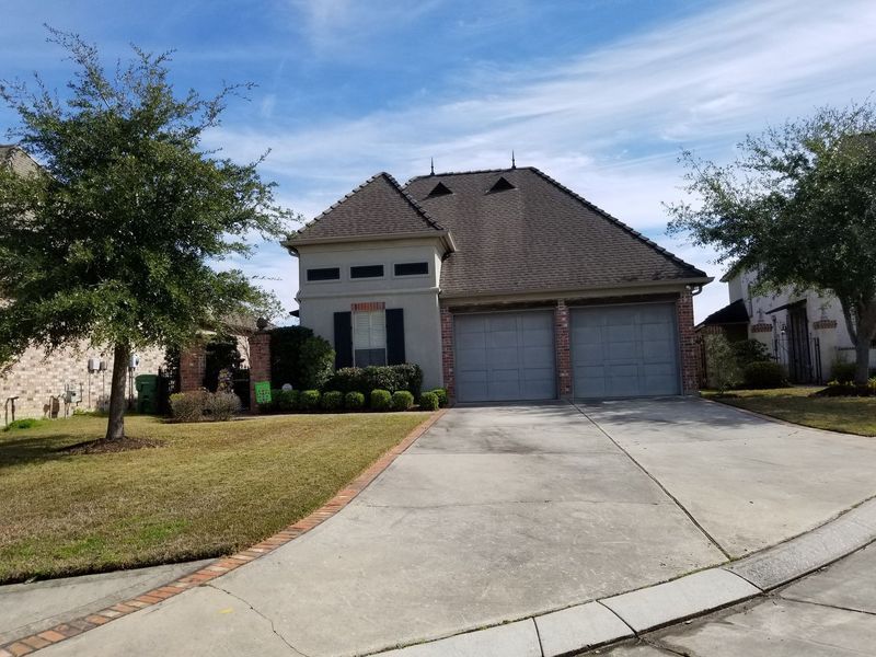 House with two-car garage, gray exterior, brown roof, driveway, trees, and blue sky.