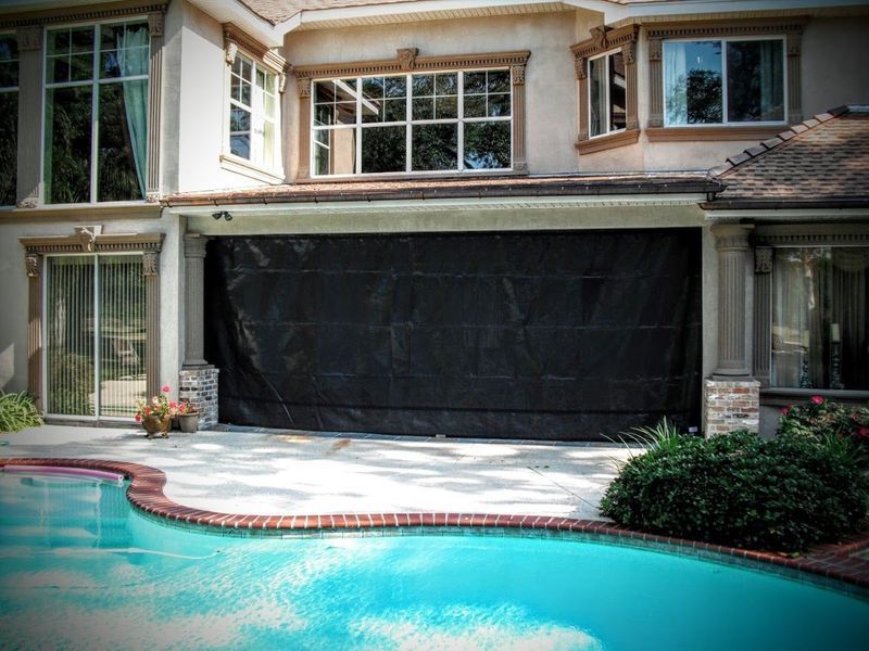 A black screen covers a garage door on a house next to a swimming pool.