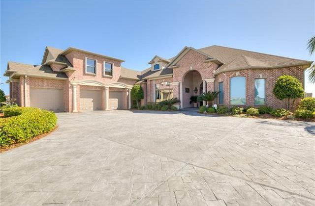 Large brick house with arched entryway and three-car garage on a patterned concrete driveway.
