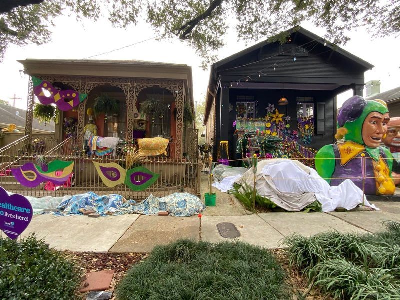 Two houses decorated for Mardi Gras with purple, green, and gold decorations; one with a pavilion and one with a dark facade.