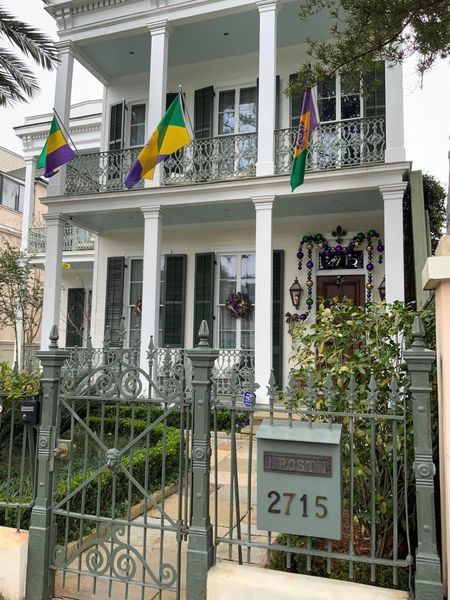 Elegant white house with Mardi Gras flags, wrought iron fence, and address 2715.