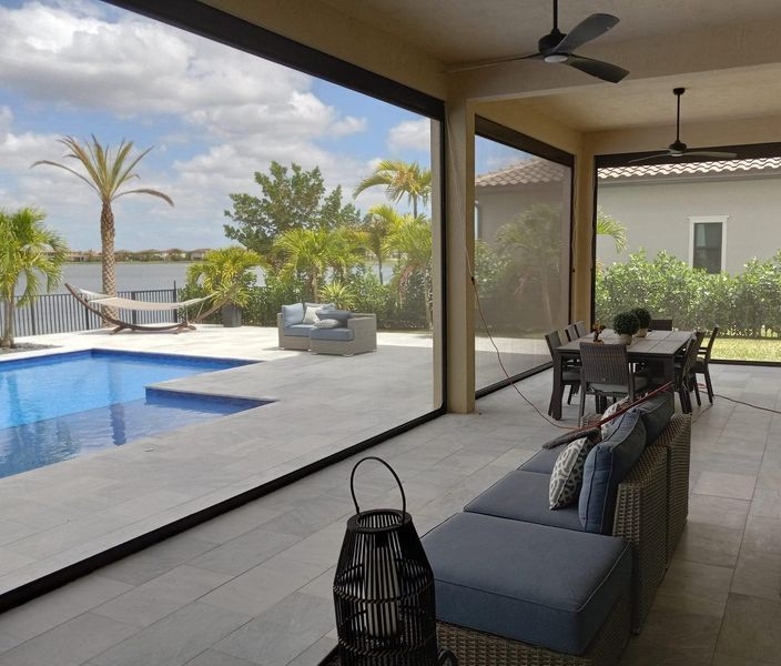 Patio with retractable screens overlooking a pool, lake, and palm trees. Furnishings are visible.