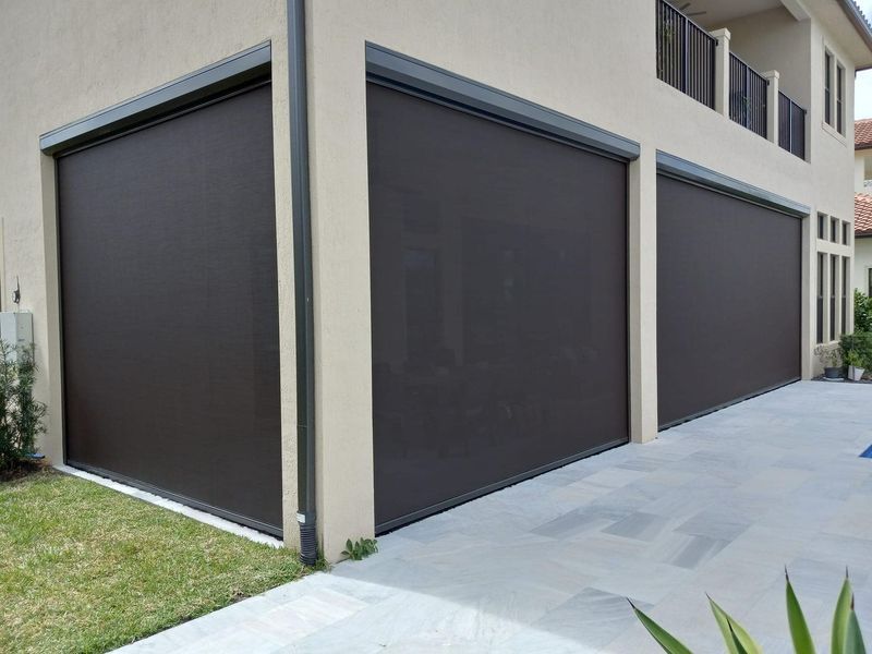 Brown outdoor roller shades covering openings in a beige house.