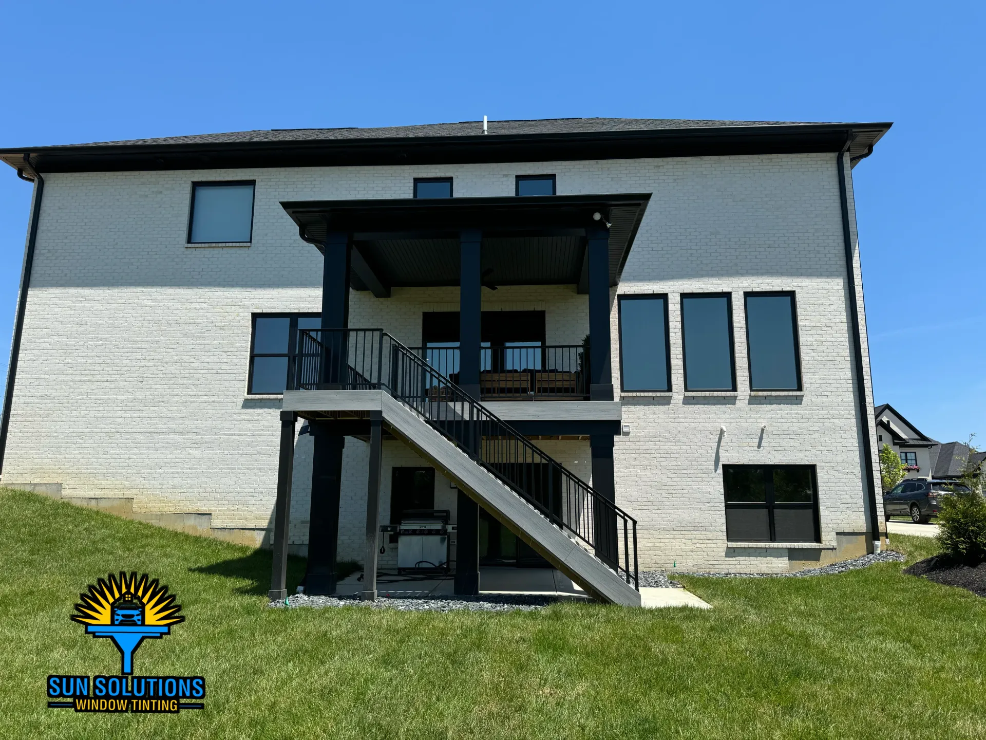 Brick house exterior with a black roof and white-framed windows, shrubbery, and a wall clock.