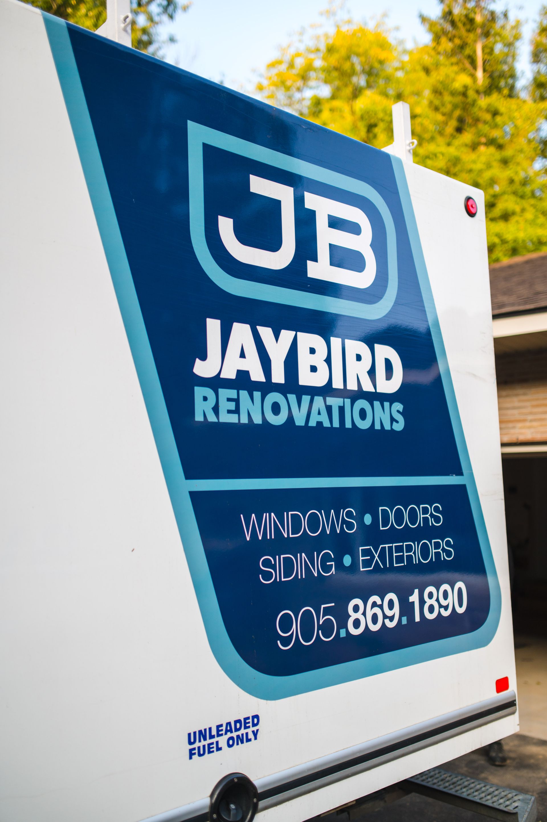A trailer for jaybird renovations is parked in front of a garage.