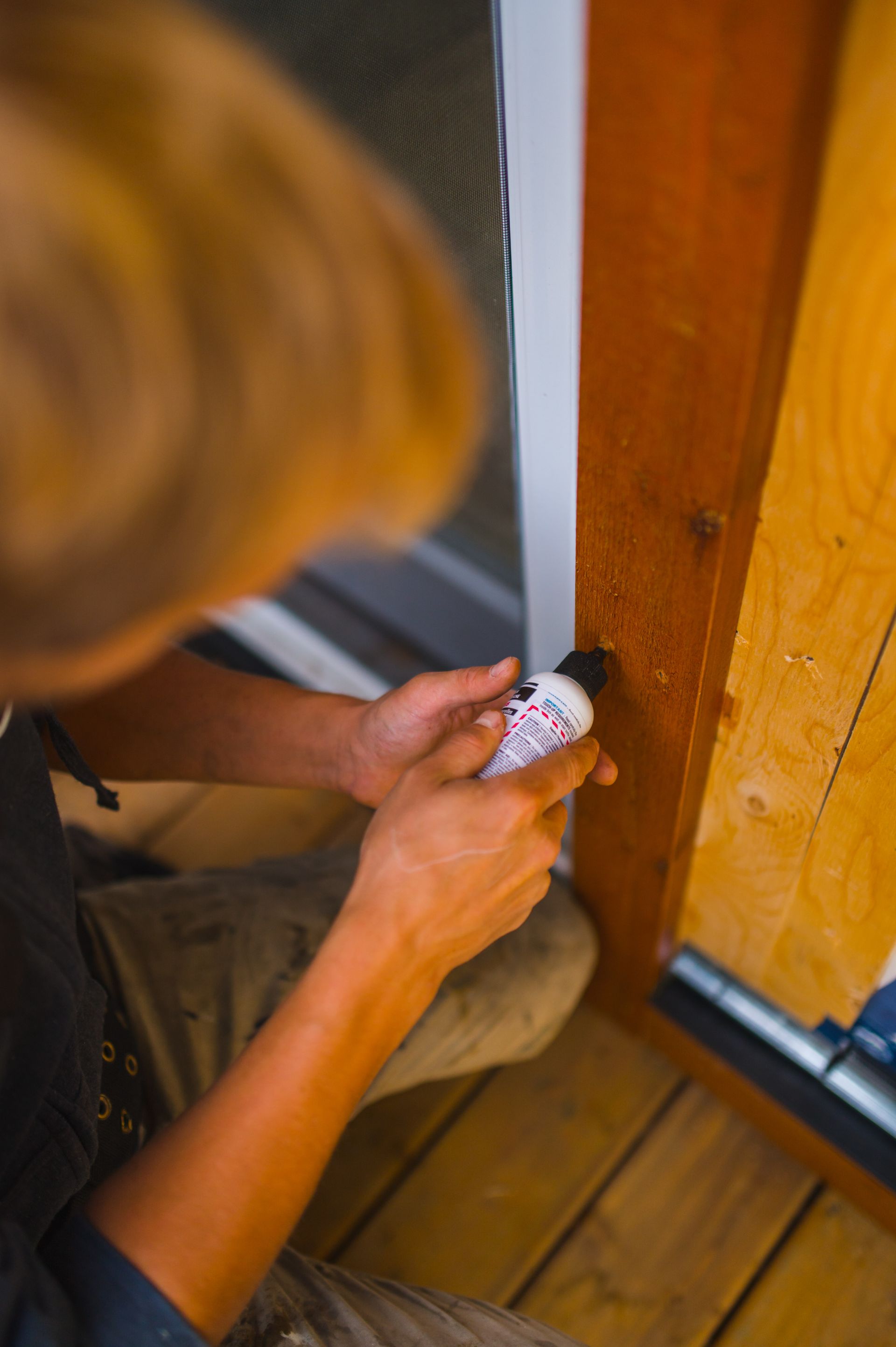 A man is using a bottle of glue to fix a door.