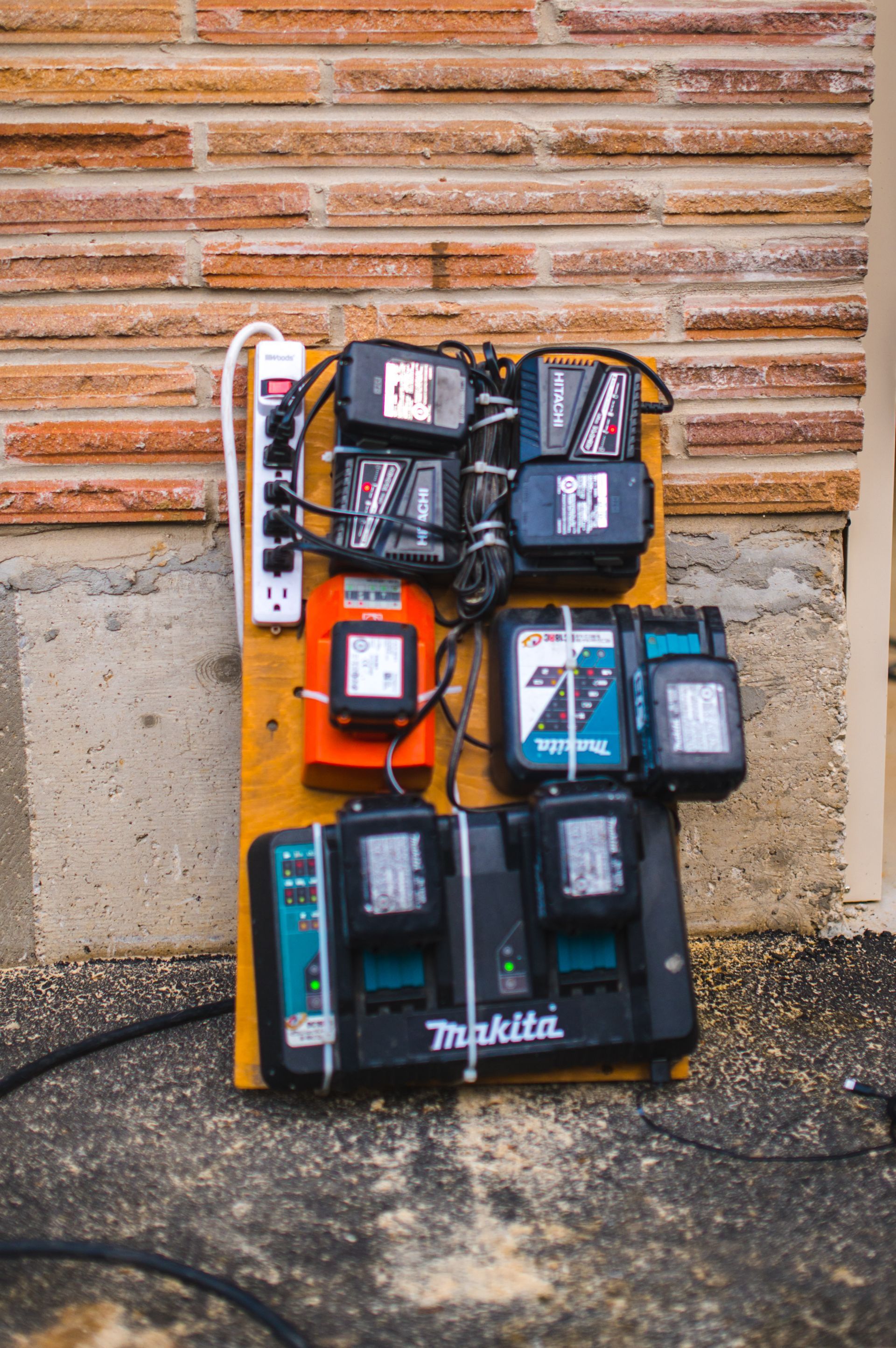 A bunch of chargers are sitting on a wooden board in front of a brick wall.