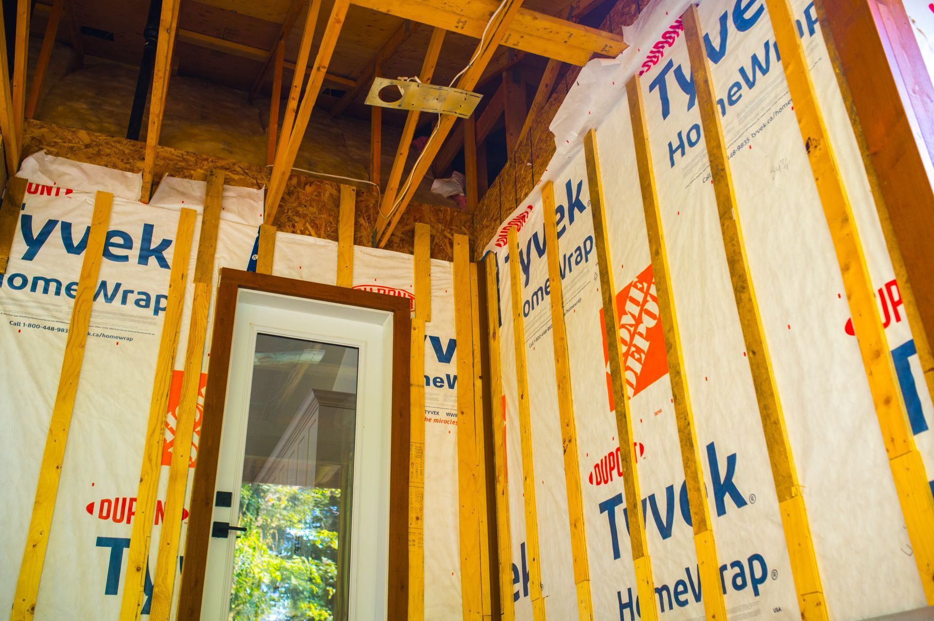 A house under construction with a door and a wall covered in tuck home wrap.