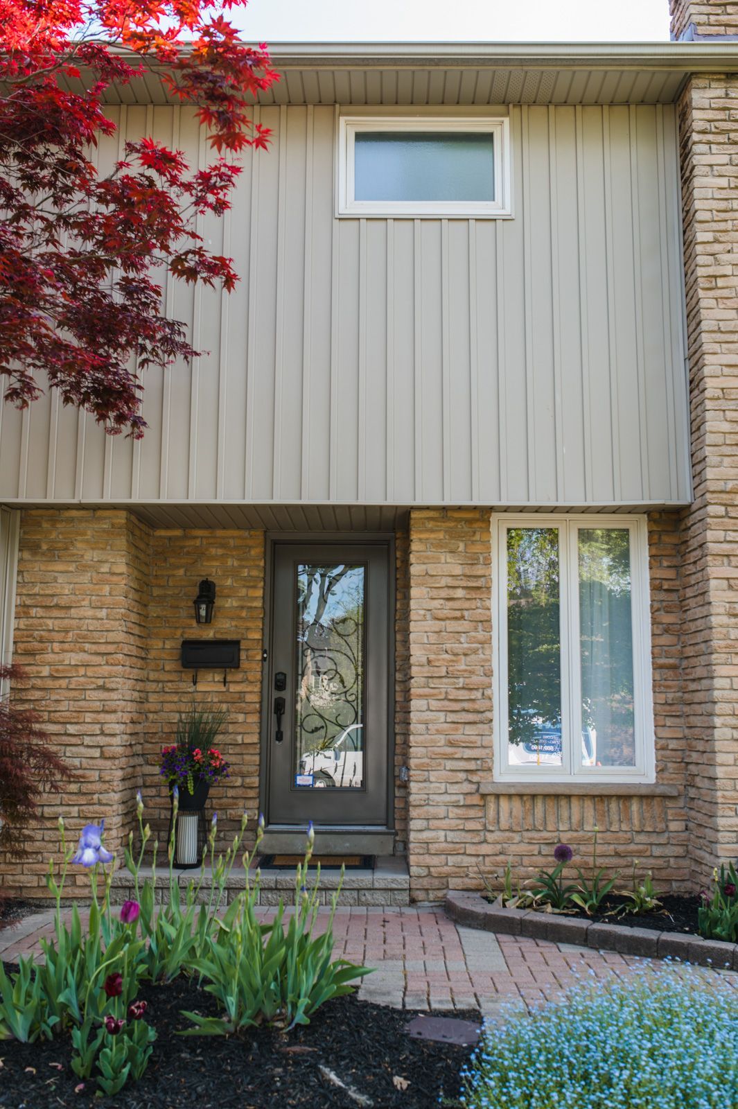 The front of a brick house with a gray door and white windows.