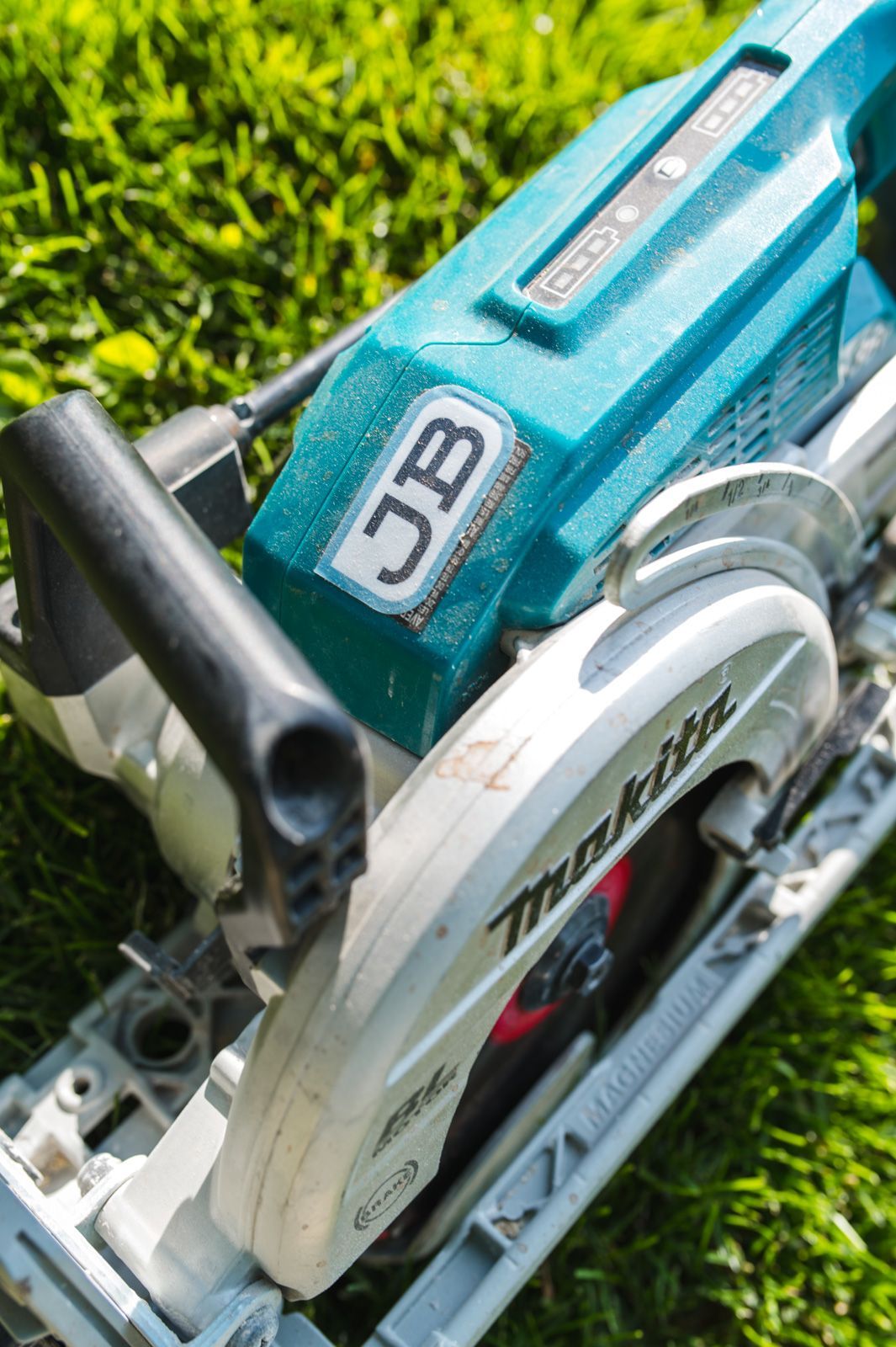 A makita circular saw is sitting on top of a lush green field.