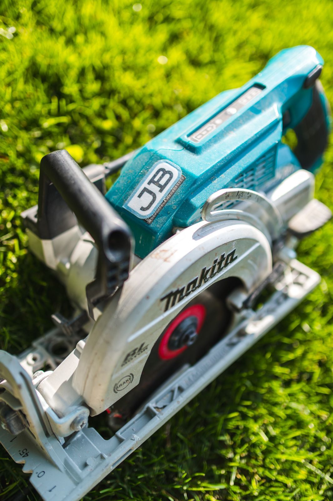 A makita circular saw is sitting on top of a lush green field.
