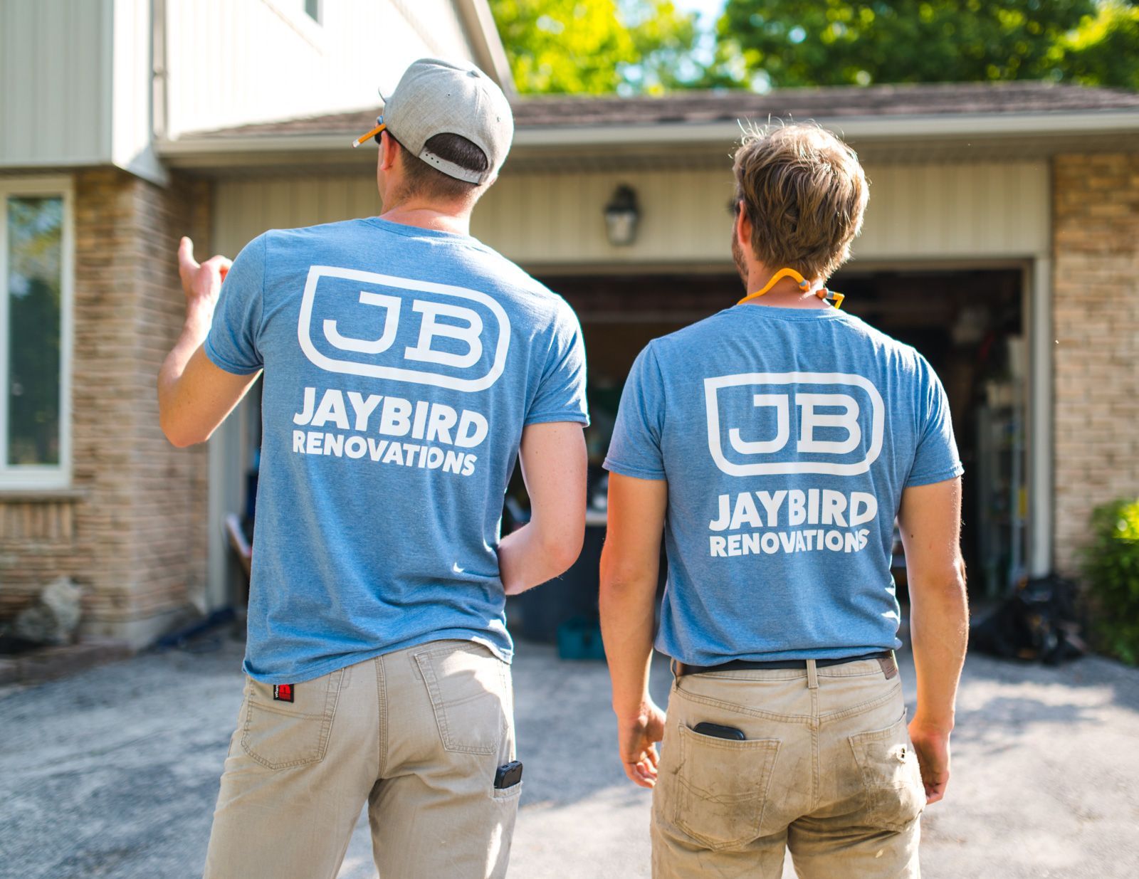 Two men wearing blue jaybird renovations shirts are standing in front of a house.