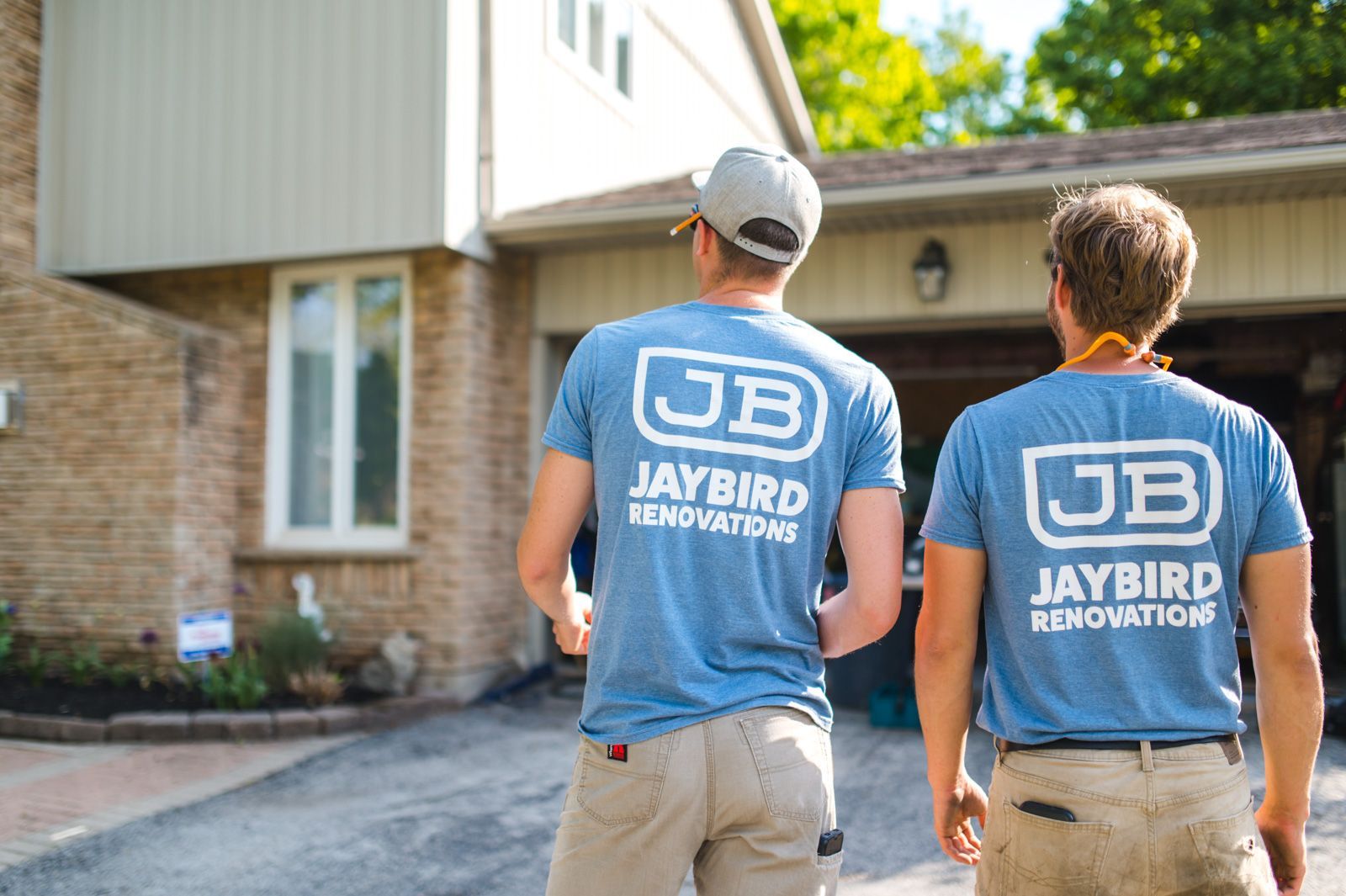 Two men wearing jaybird t-shirts are walking in front of a house.