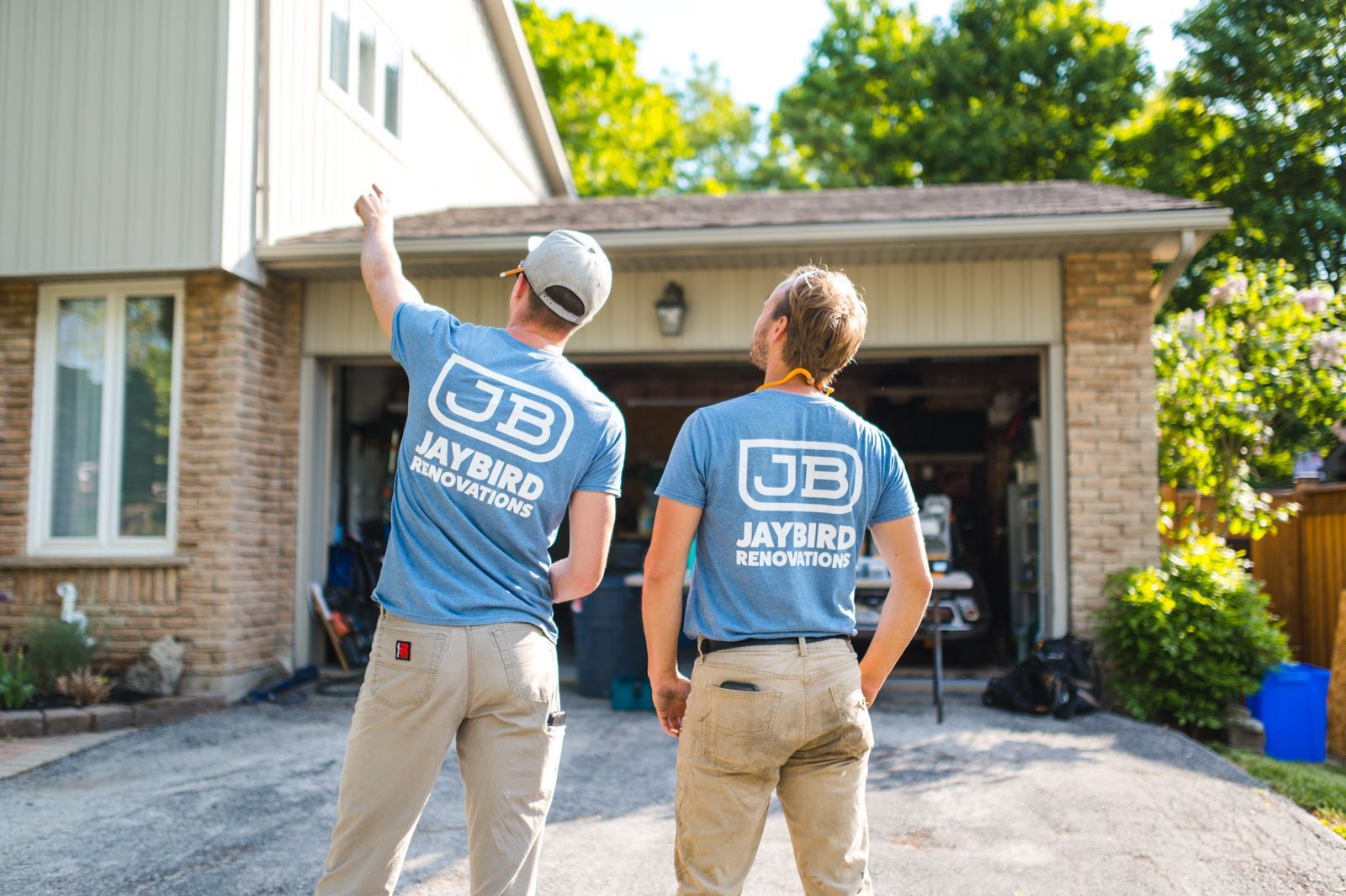 Two men in blue shirts are standing in front of a house.